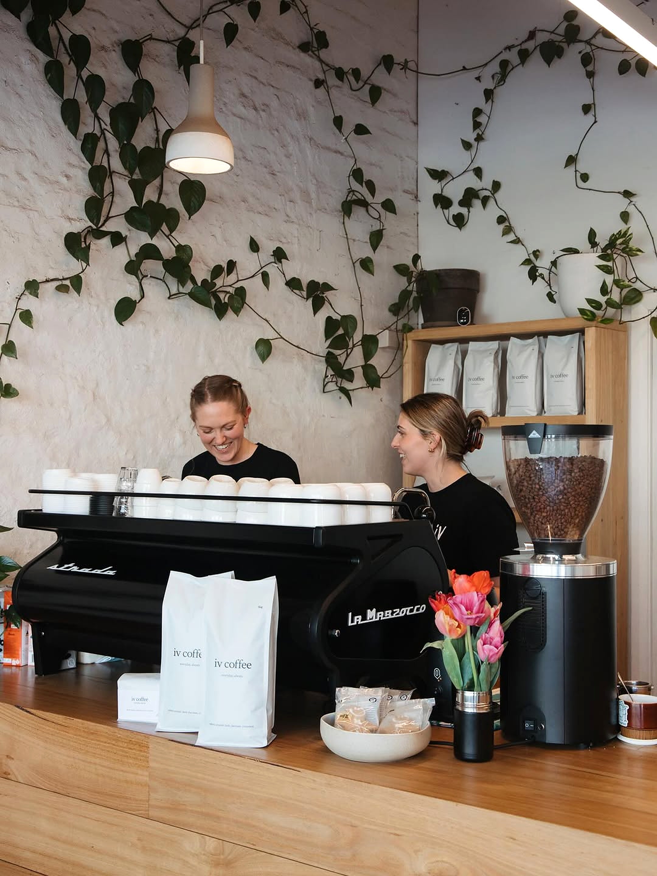 Two baristas behind the La Marzocco with iv coffee beans on the shelf behind